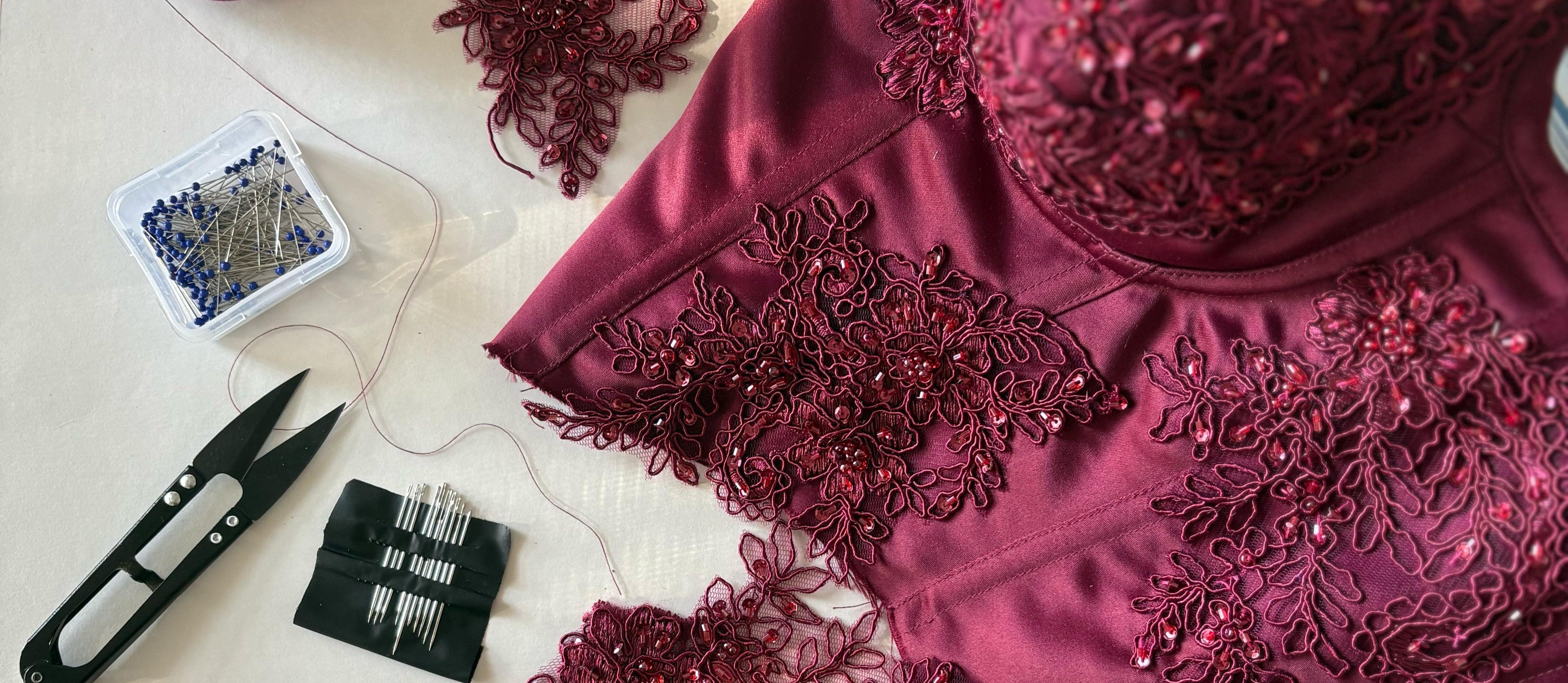 Maroon embroidered fabric with lace details on a white surface, surrounded by sewing tools.