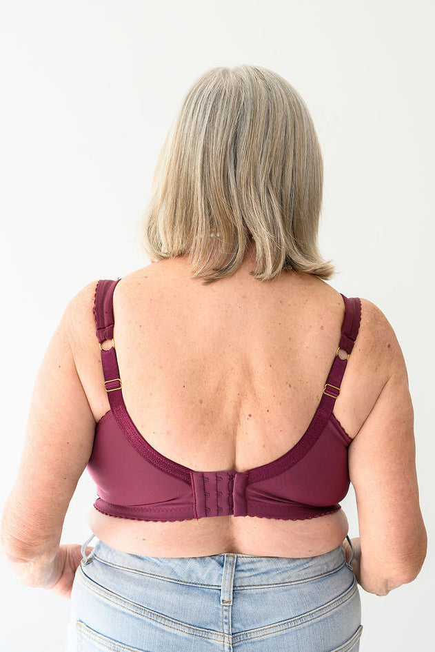 Back shot of a person wearing a black cherry bra by Rubies Bras with light blue jeans on a white background