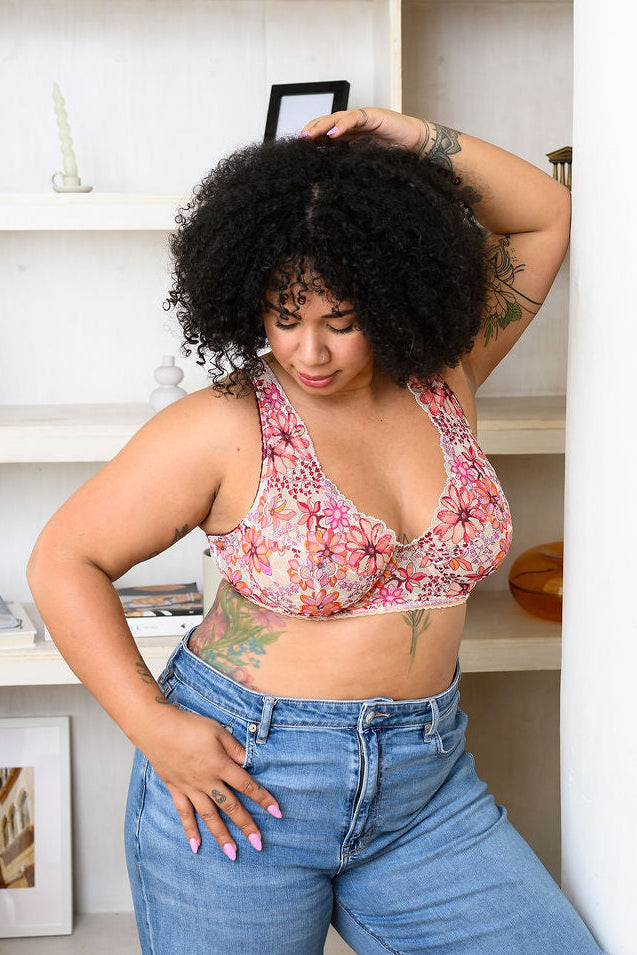 Woman in a floral lace bra and jeans standing in front of a bookshelf.