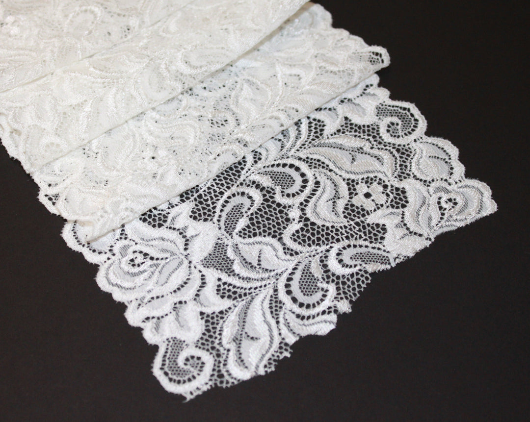 White scalloped lace fabric with a floral pattern displayed on a flat surface. Rubies Custom Bras.