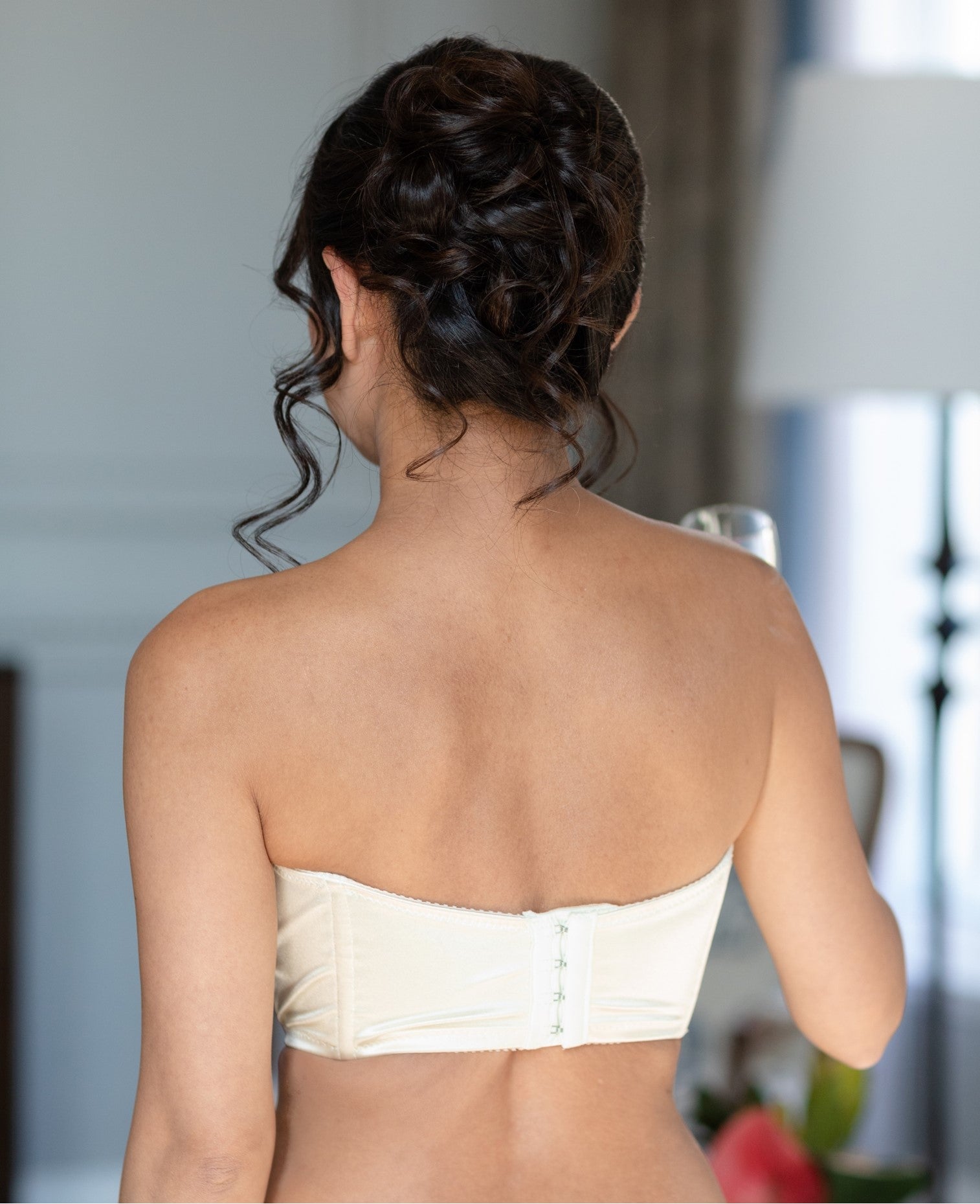 A bride with black hair in an updo with her back turned to the camera wearing a strapless white bustier from Rubies Custom Bras.