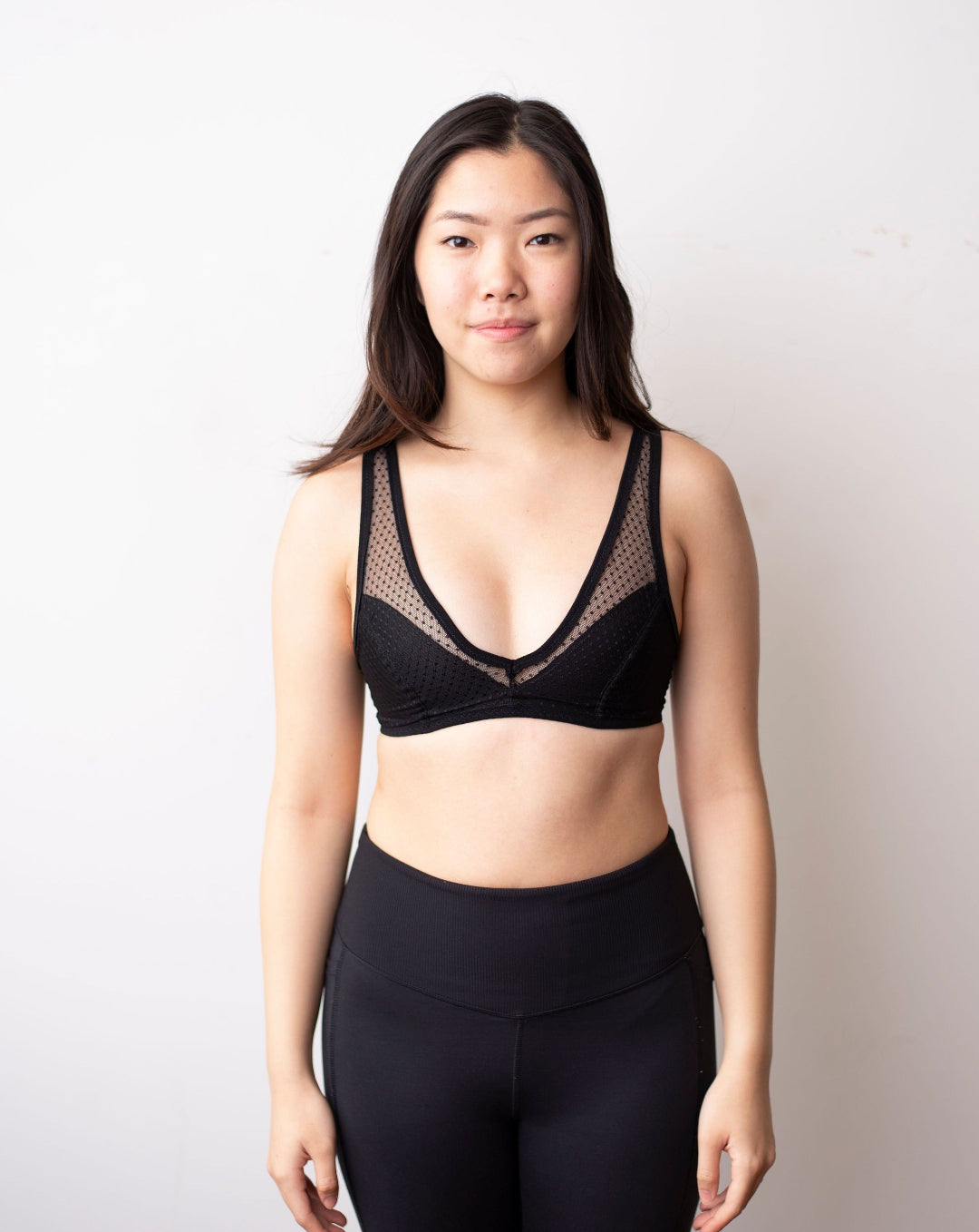 Rubies Bras. Female with long black hair wearing a black dotted lace wirefree bra with deep plunge v neckline. Front facing full body shot on white background.