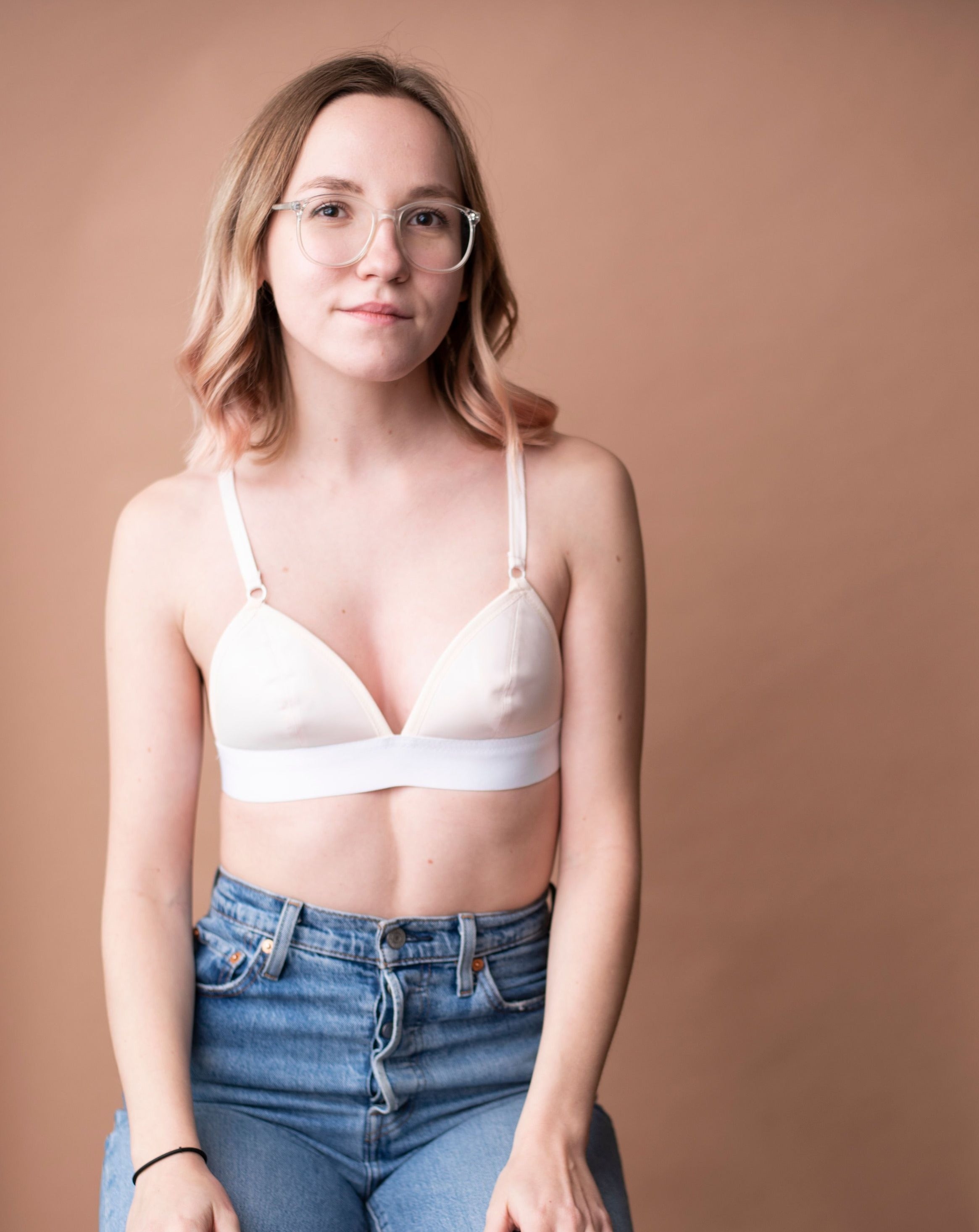 Haley from Rubies Bras, a female with medium blond hair wearing a peach and white wirefree bra from our petites collection styled with blue jeans. Half body shot on copper back drop.