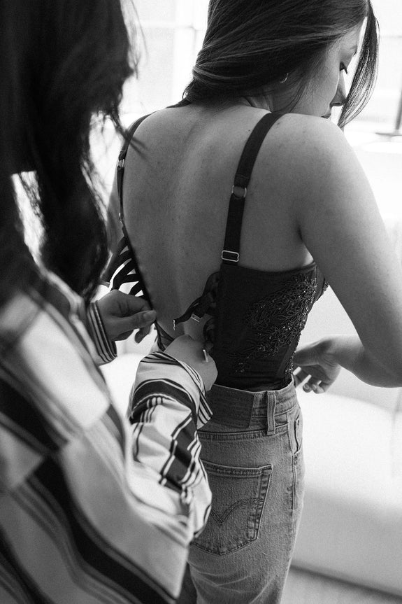 Bra specialists assists client lacing up custom lingerie.