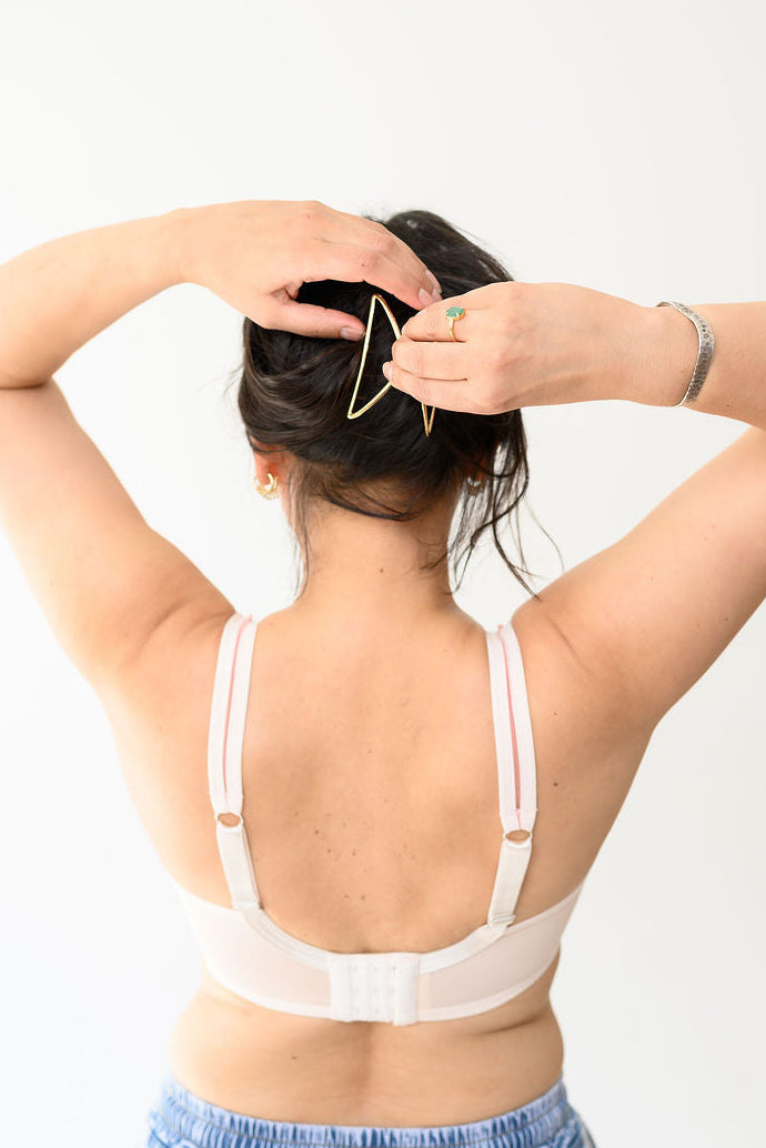 Person wearing a peach bra and blue jeans with hands behind head on a white background