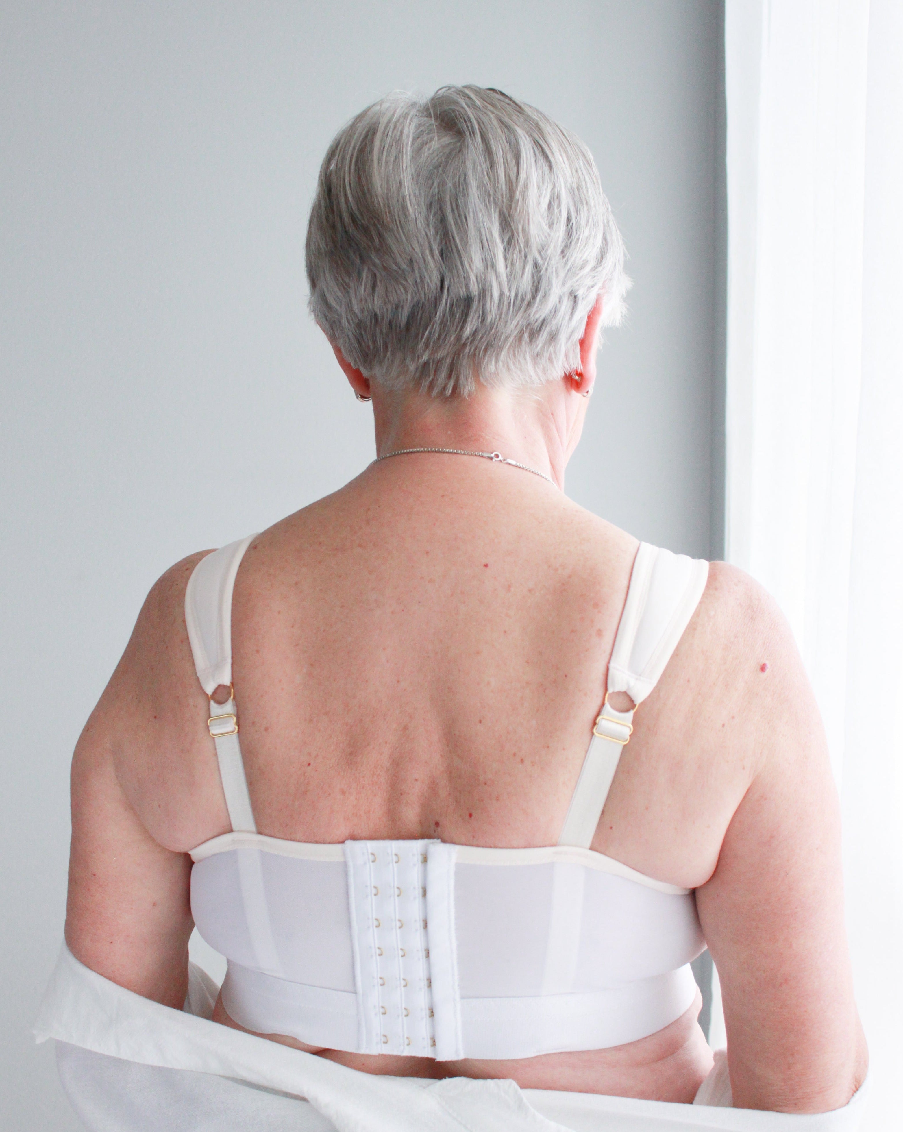 The back of a woman with short grey hair wearing a white, full coverage, wired Ingrid Bra from Rubies Custom Bras.