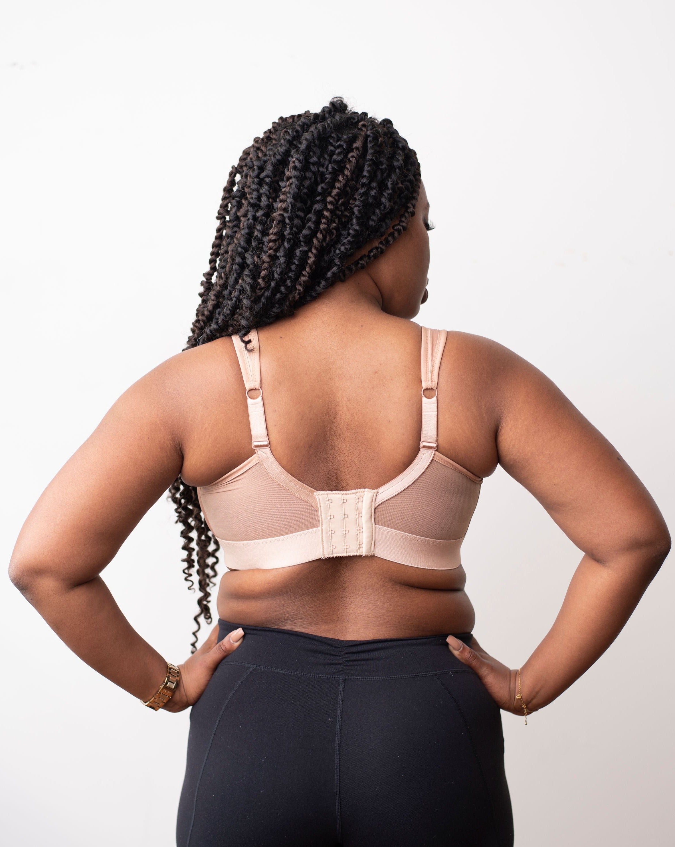 The back of a model with black braids wearing a beige mastectomy bra. Made with low stretch and wide elastics for comfort and support. Can add your own prosthesis or we can sew them in. 