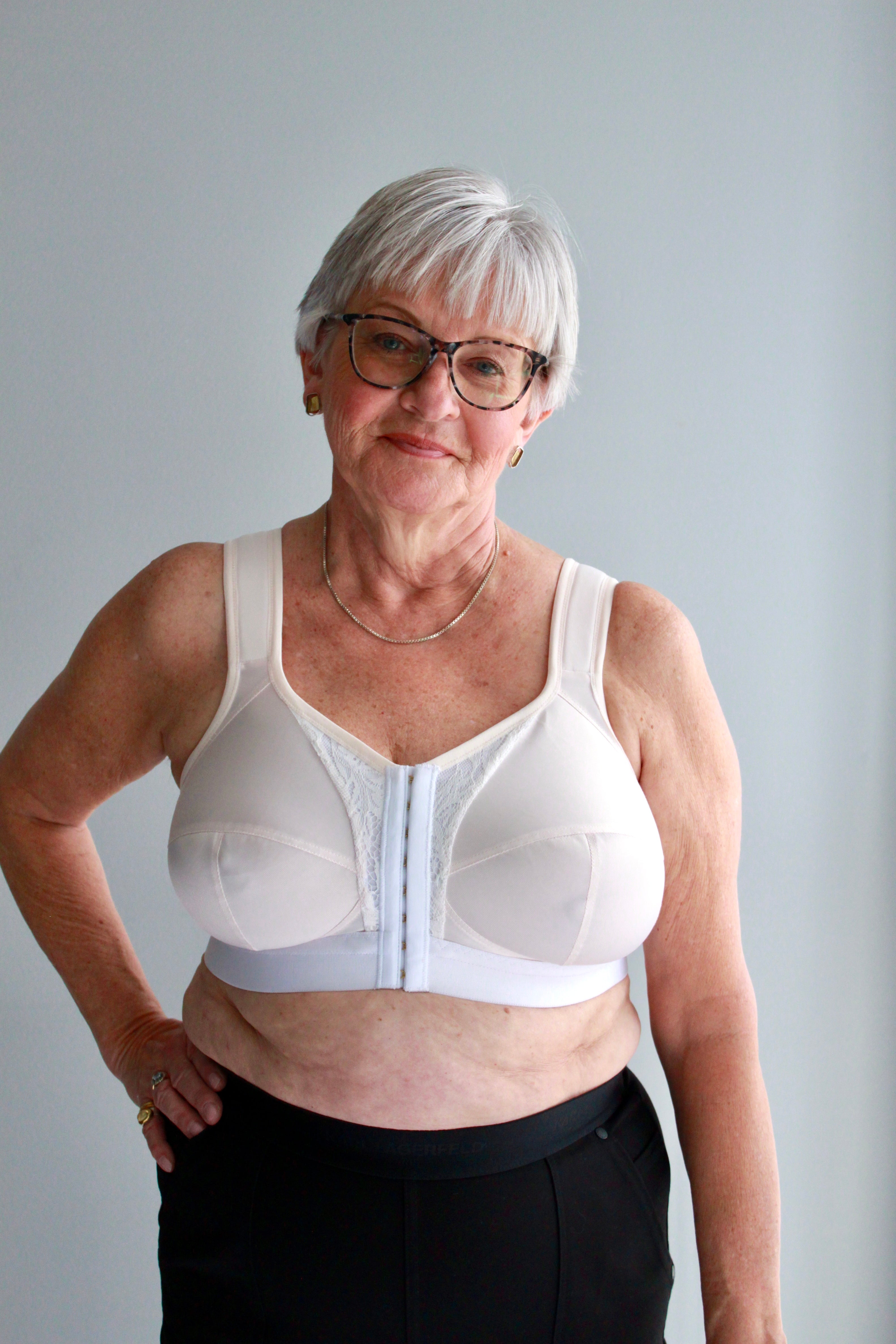 A model with short grey hair wearing a peach and white mastectomy bra. Made with low stretch and wide elastics for comfort and support. Can add your own prosthesis or we can sew them in. 