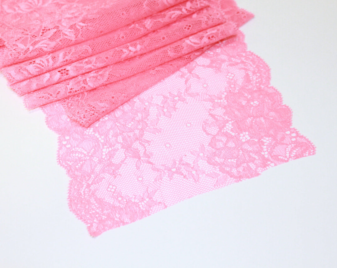 Pink scalloped lace fabric with a floral pattern displayed on a flat surface. Rubies Custom Bras.