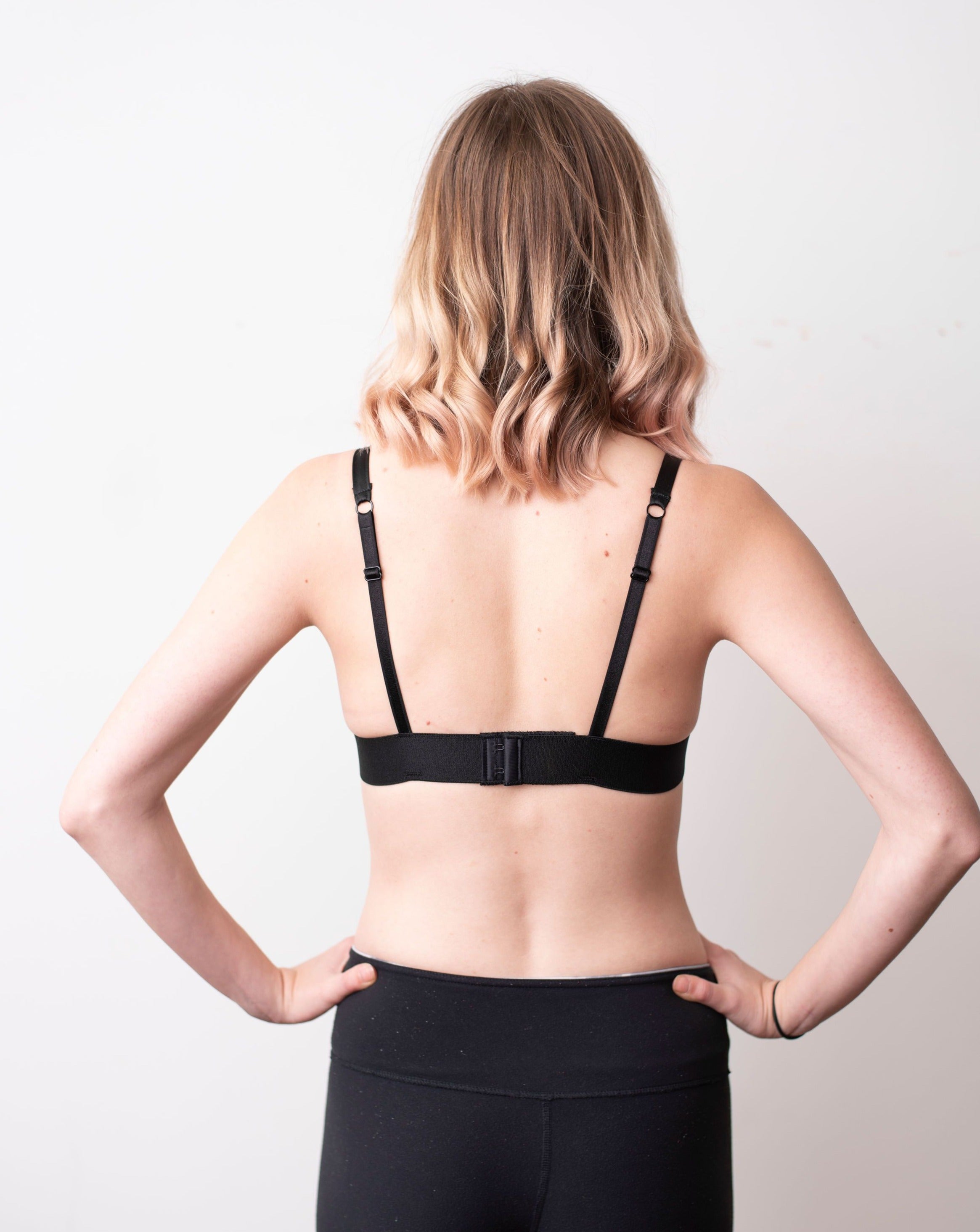 Haley from Rubies Bras, a female with medium blond hair wearing a black scalloped lace wirefree bra from our petites collection. Full back body shot on white back drop.