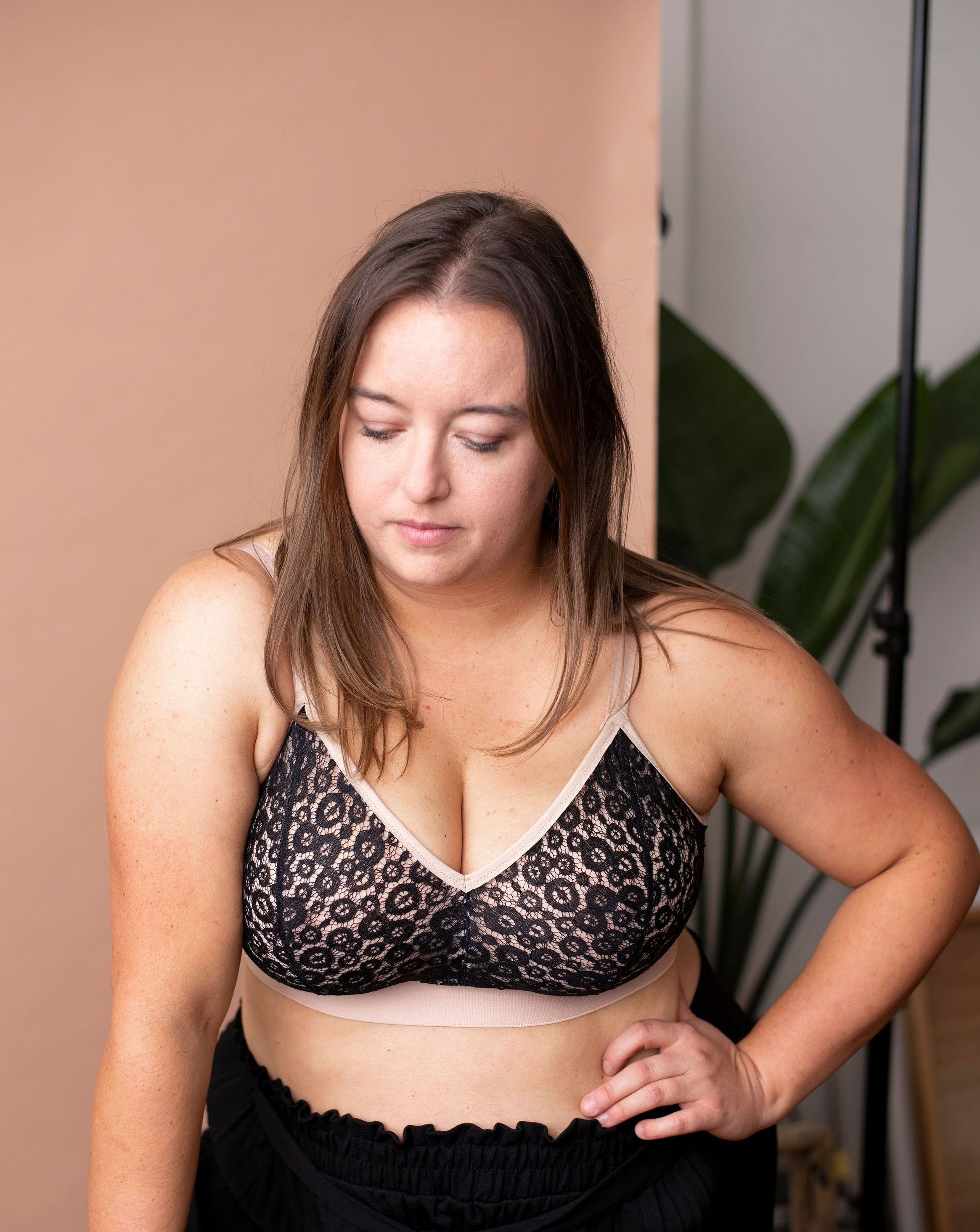 Model wearing poppy lace bra from Rubies Custom Bra and black pants against an earth tone background.