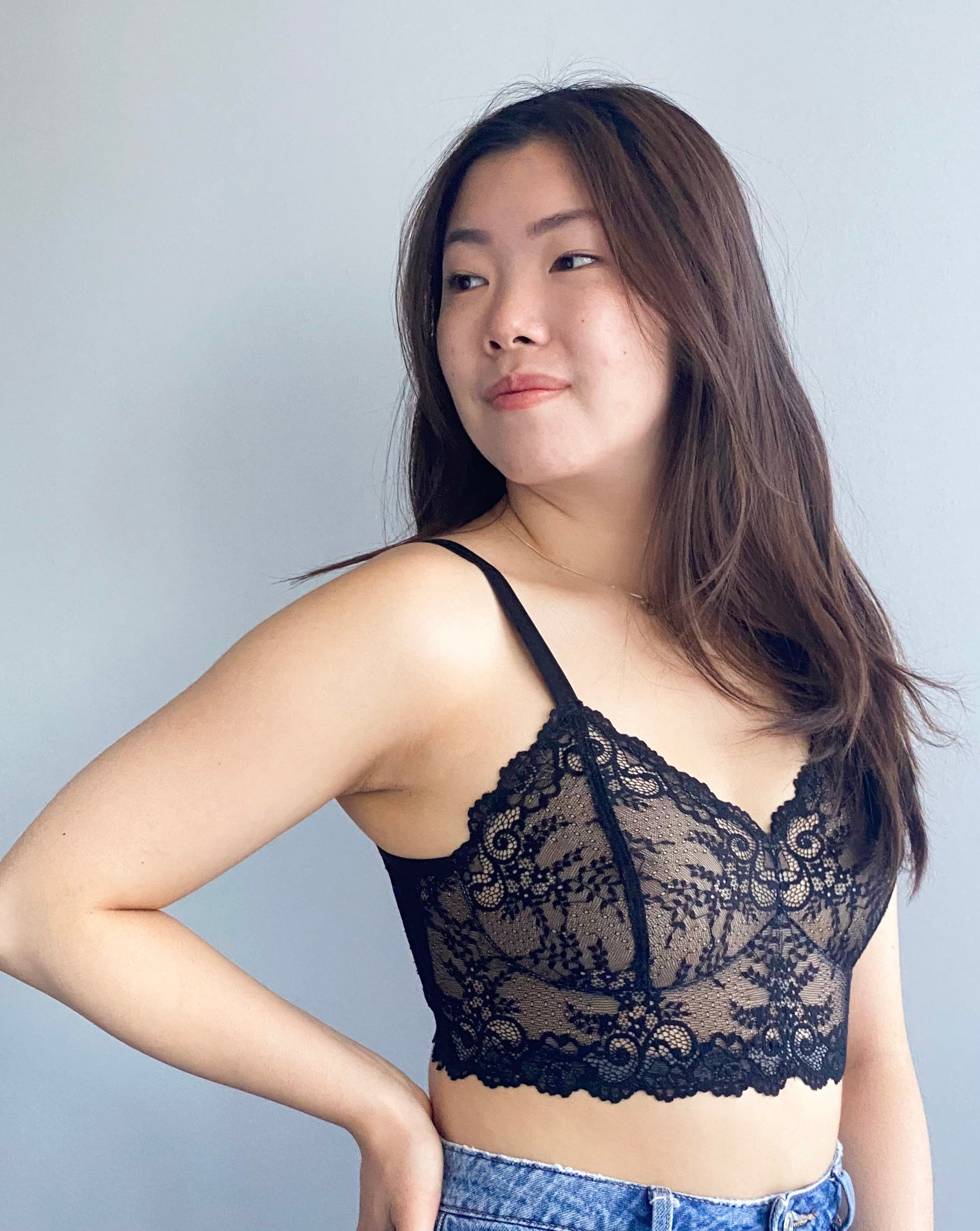 Model with long dark brown hair turning her head away from the camera with her hand on her hip wearing a black lace Viva Scalloped wirefree Bra from Rubies Custom Bras.