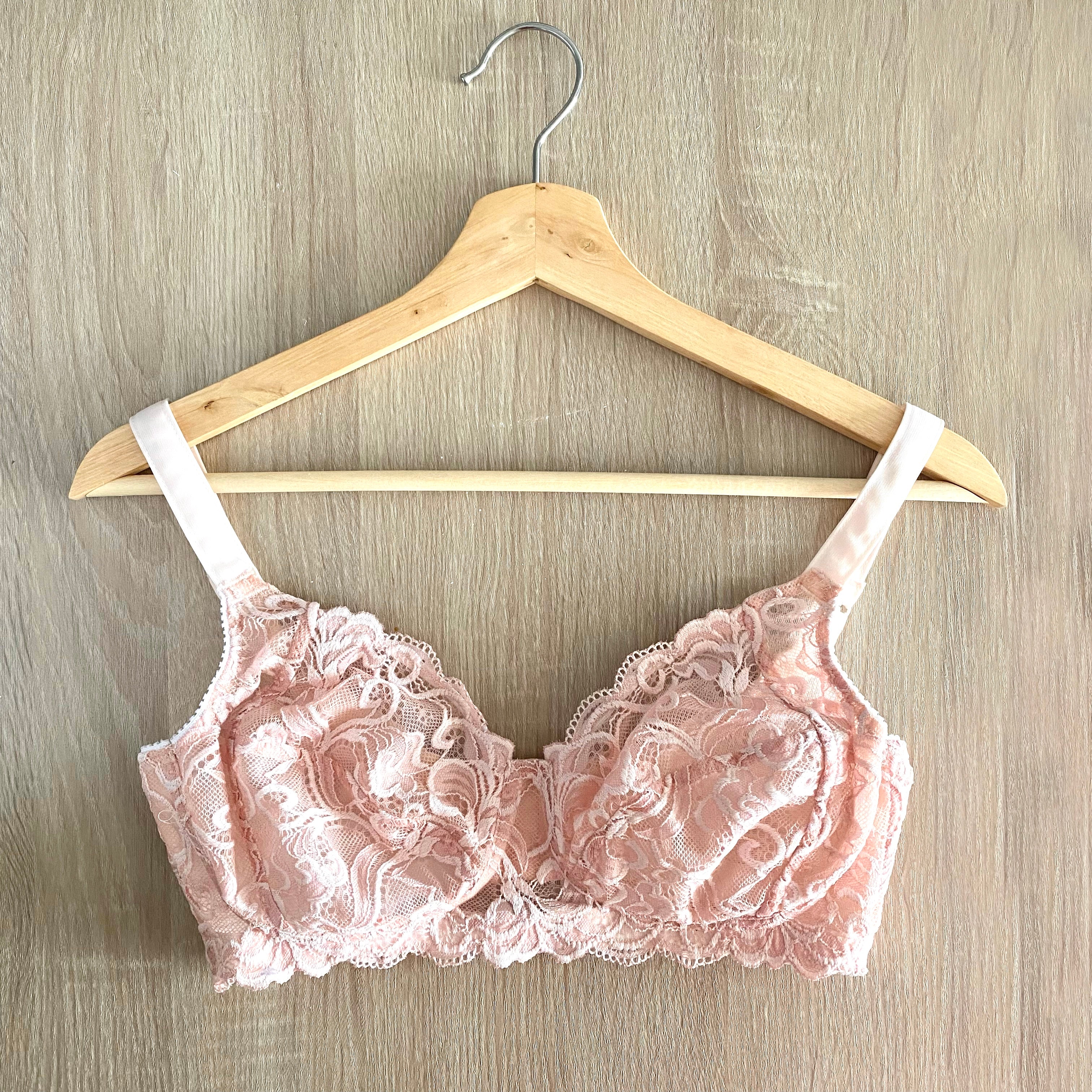 A pink wire-free bra on a hanger laying flat on a wooden surface from Rubies Custom Bras. 