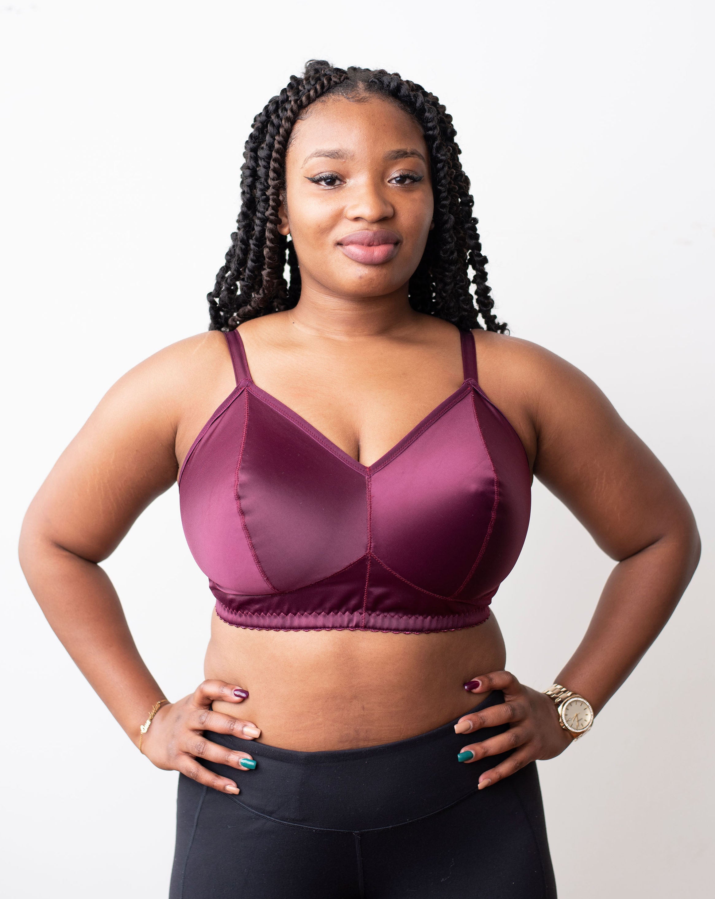 A dark-skinned model with braids, facing the camera with her hands on her hips wearing a Viva Solids bra in Black Cherry from Rubies Custom Bras. 