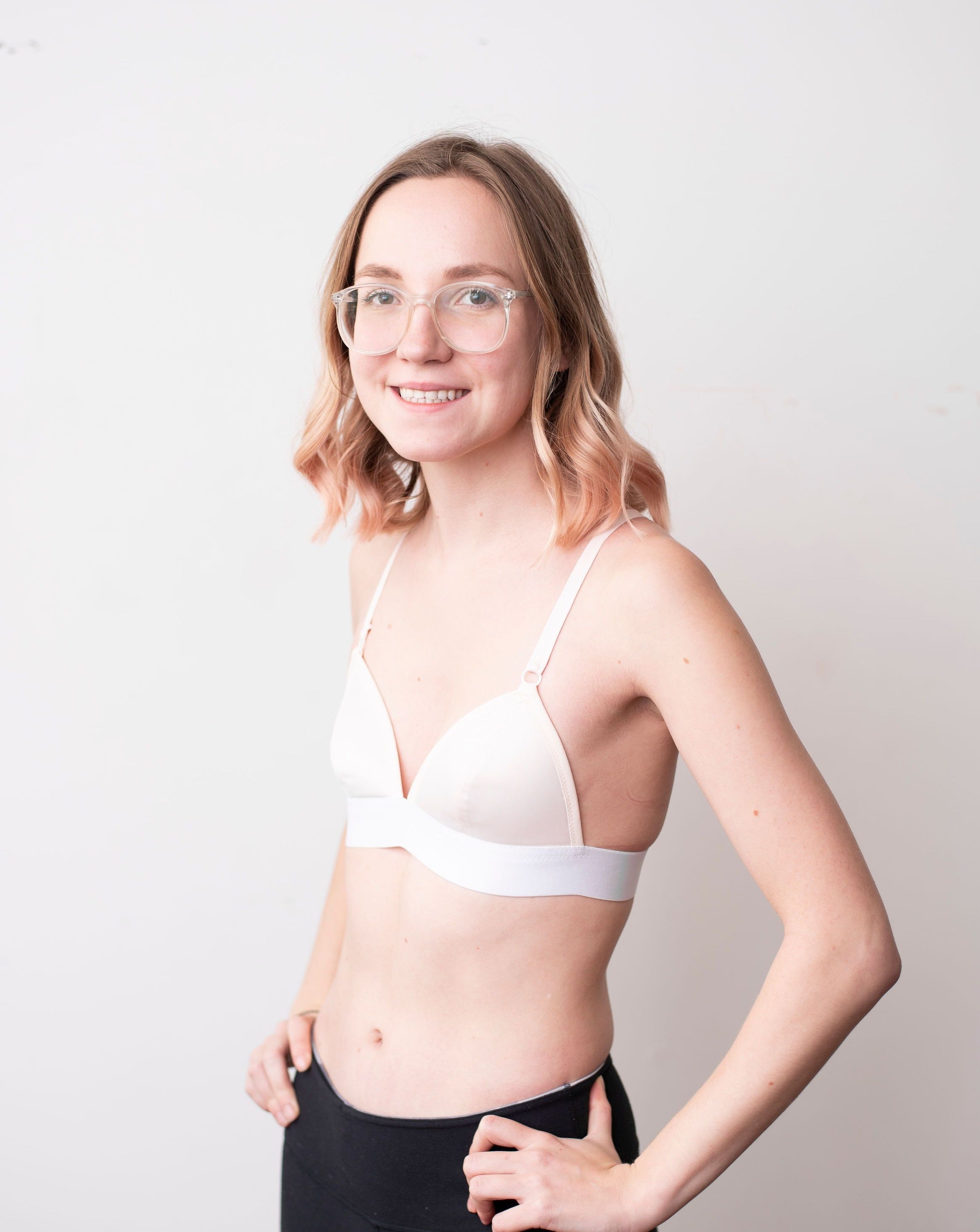 Haley from Rubies Bras, a female with medium blond hair wearing a peach and white wirefree bra from our petites collection. Side body shot on white back drop.