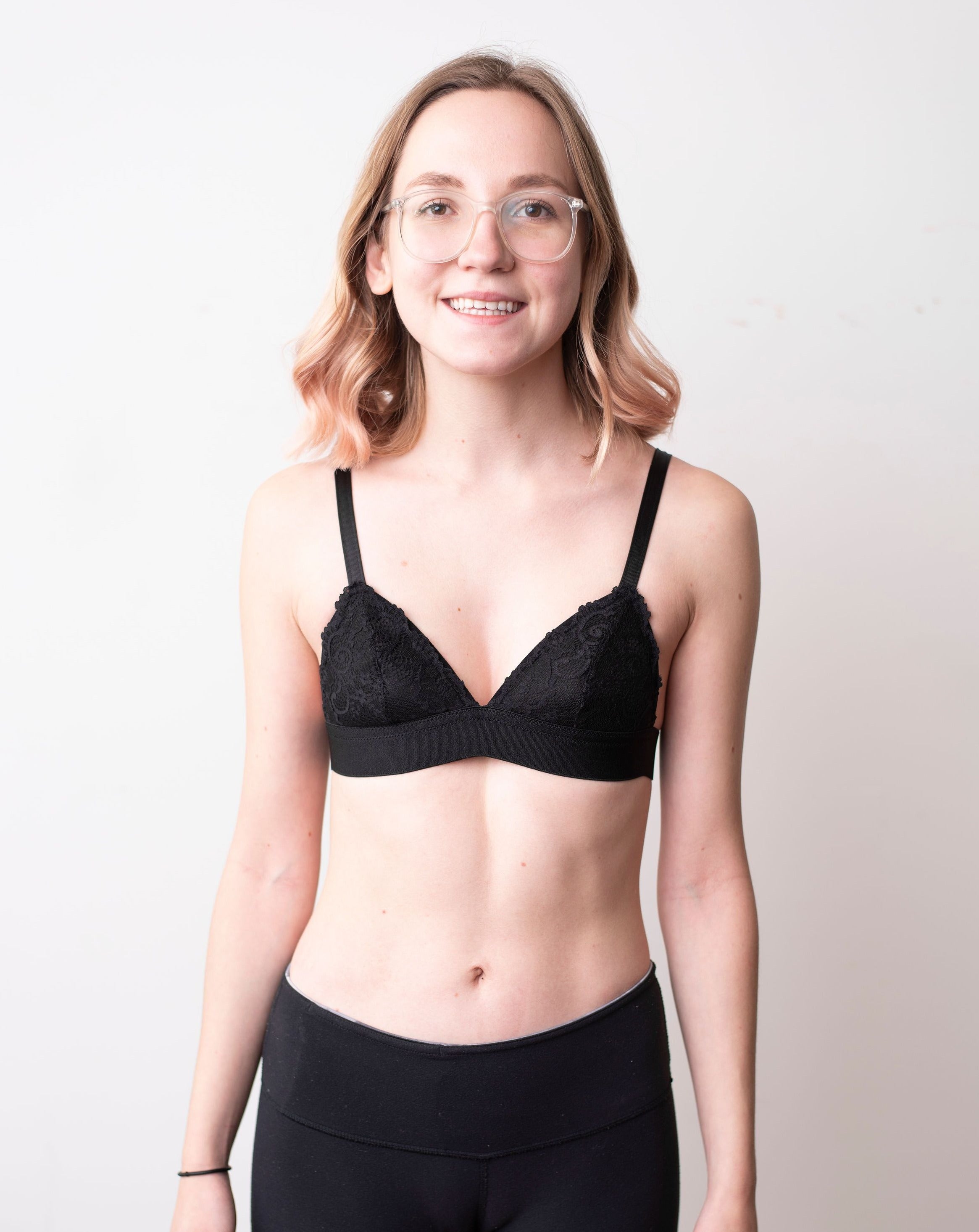 Haley from Rubies Bras, a female with medium blond hair wearing a black scalloped lace wirefree bra from our petites collection. Full front body shot on white back drop.