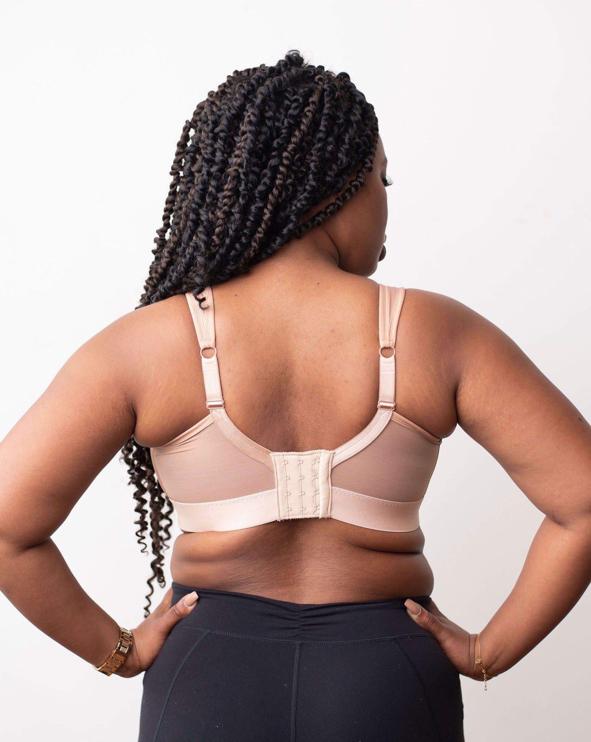 Lia from Rubies Bras, a female with long braided hair, is wearing a beige maximum solids full coverage bra. Back shot on white backdrop.
