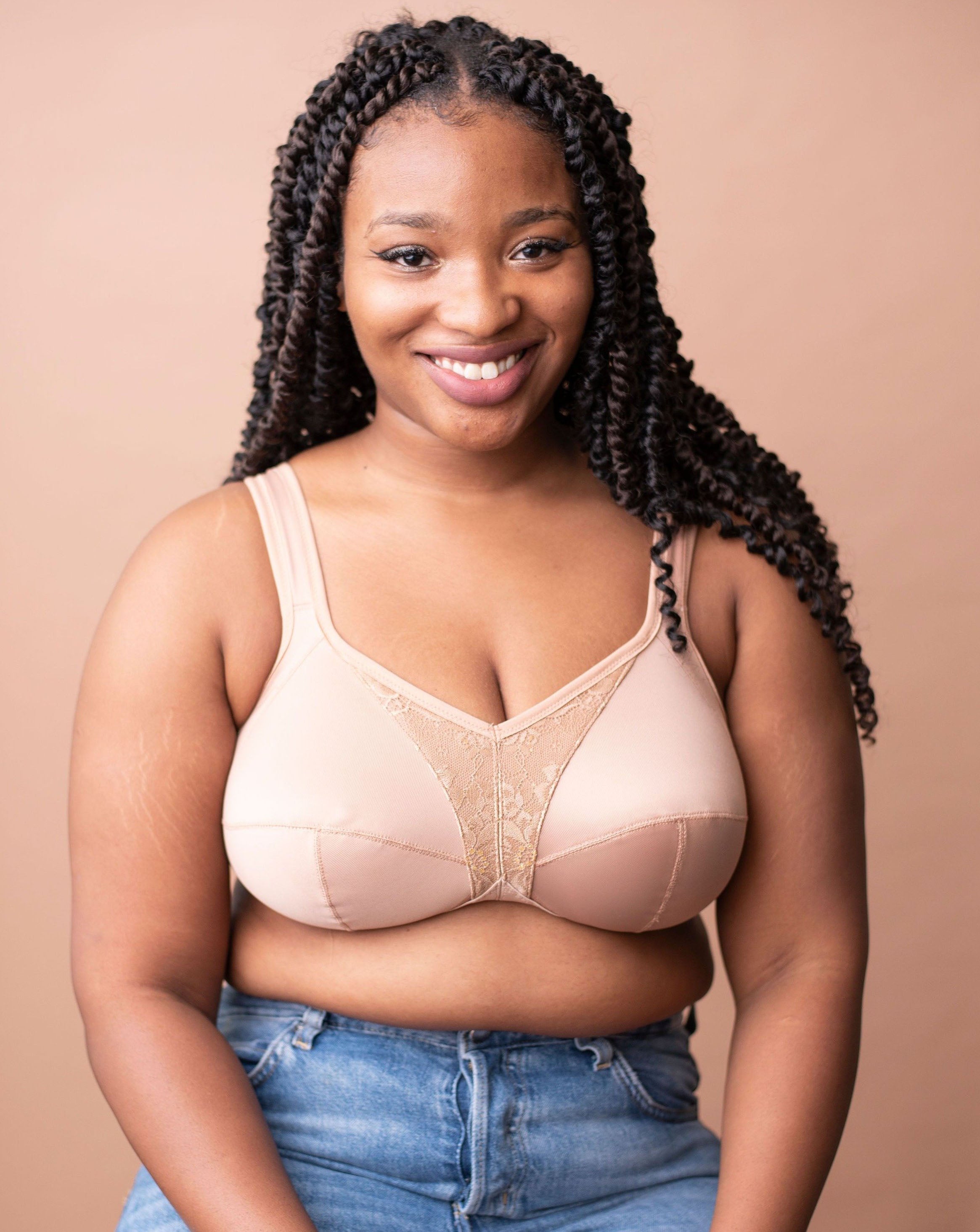 Lia from Rubies Bras, a female with long braided hair, is wearing a beige maximum solids full coverage bra and blue jeans. Shot on copper backdrop