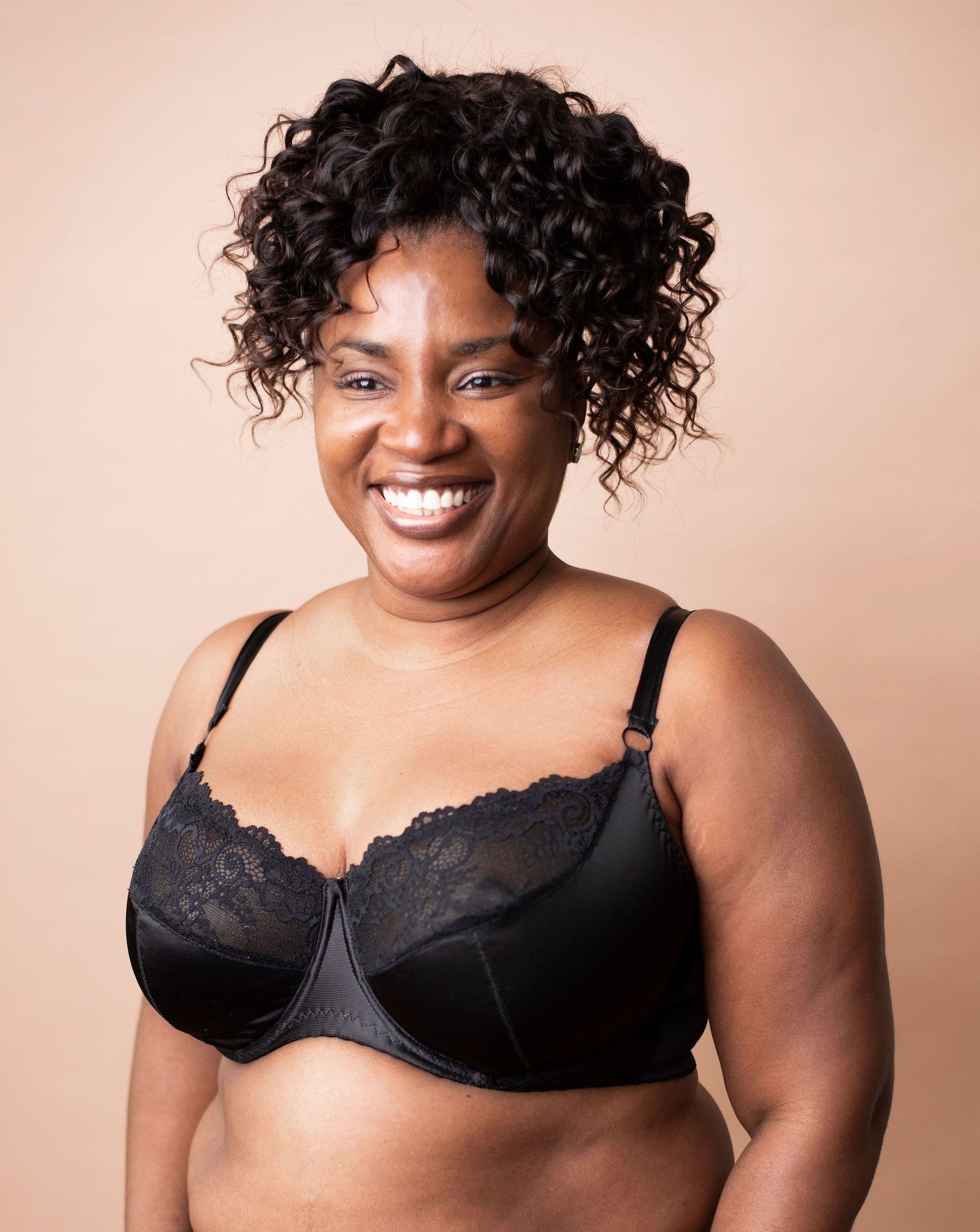 Model with dark curly hair is wearing a custom black wired bra. Half body frontal shot in front of a copper background.