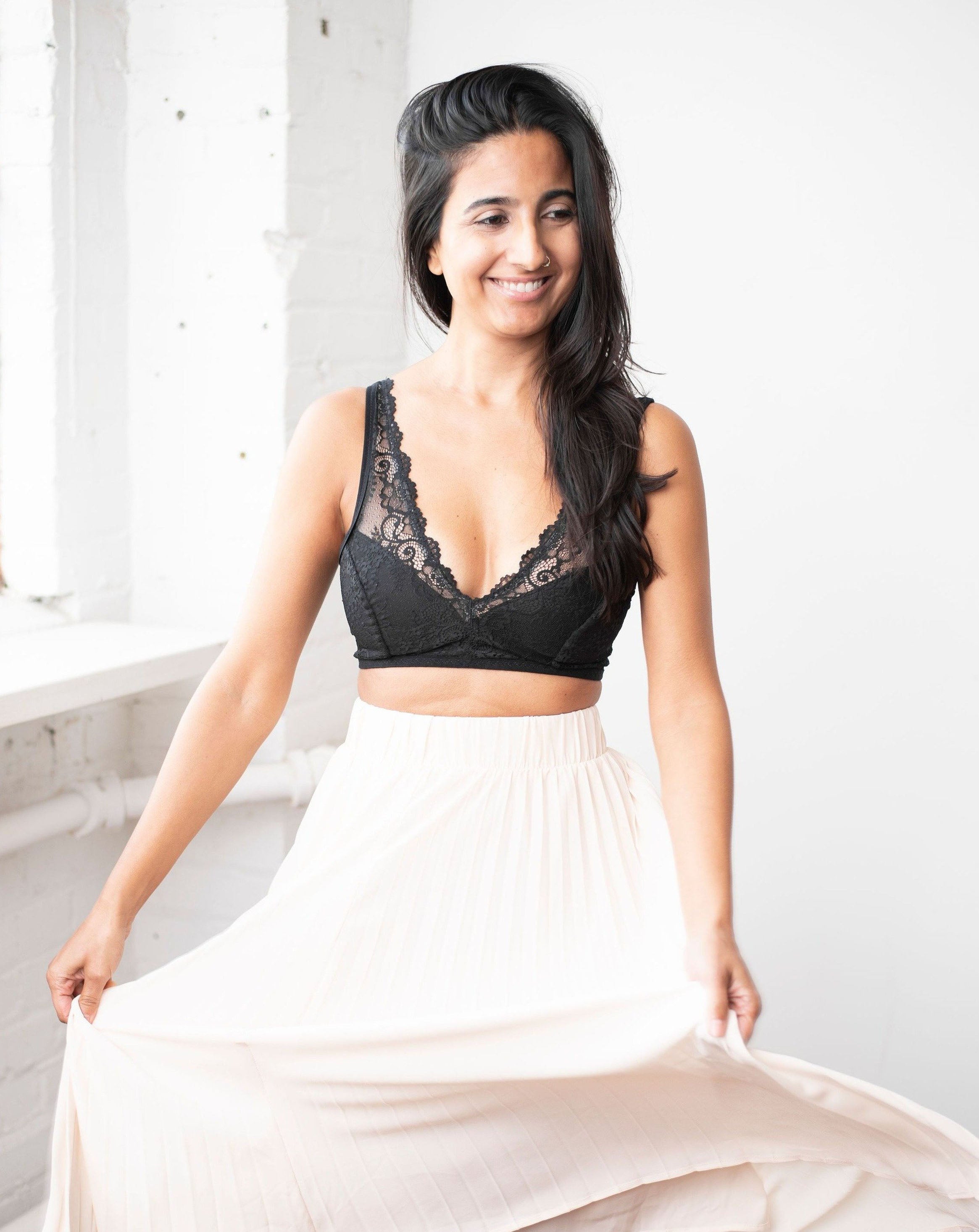 Ruhee with Rubies Bras, a female with long black hair wearing a black scalloped lace wirefree bra with deep plunge v neckline. Full front body shot on white back drop.