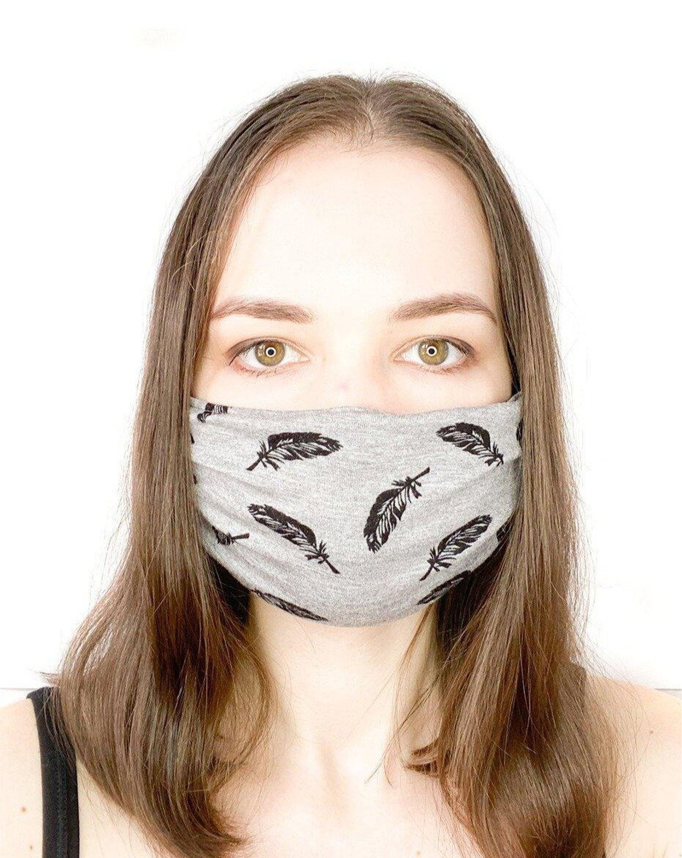 Model with brown hair wearing a black feather on grey organic cotton facemask.