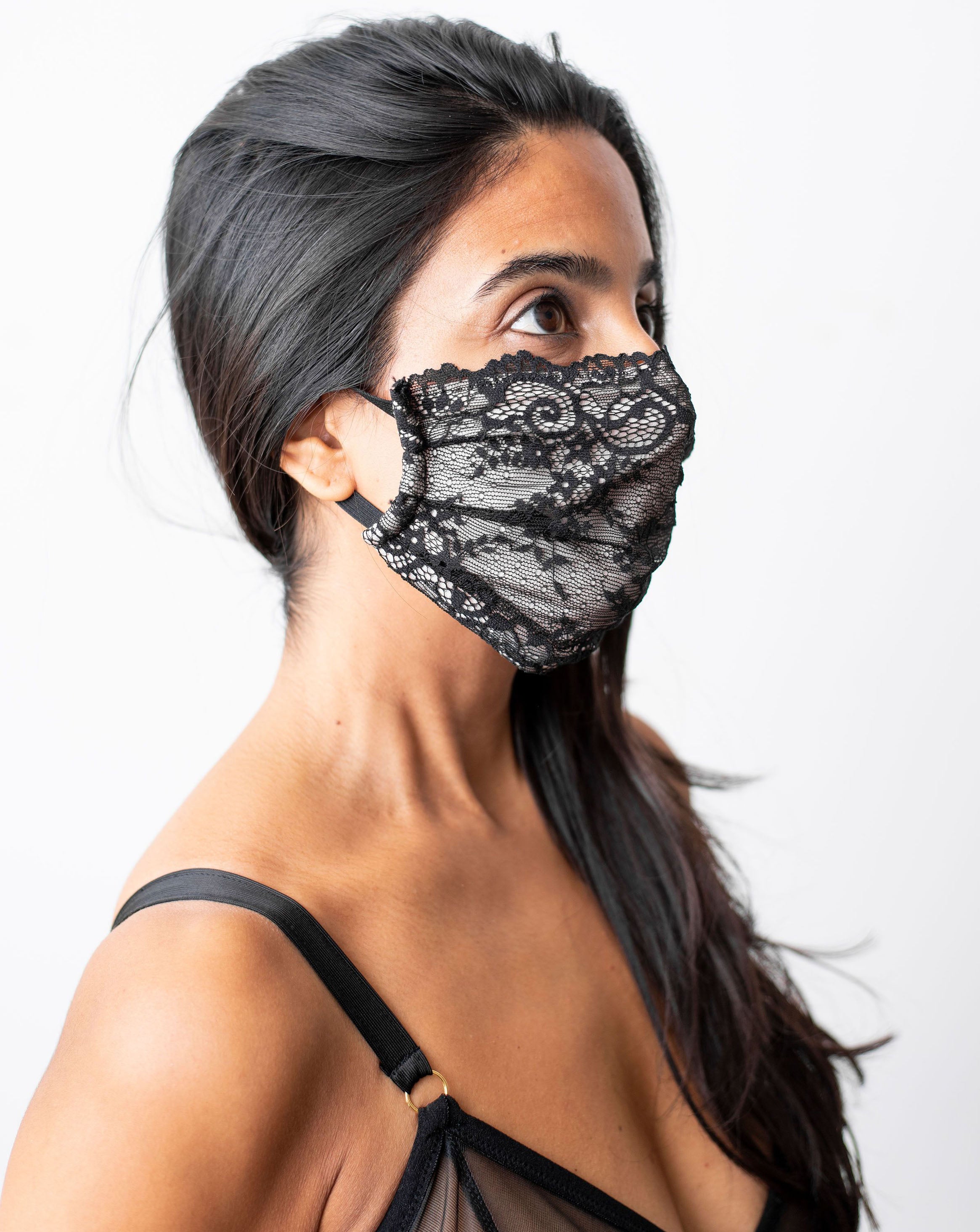 Ruhee, female with long black hair wearing a black lace, organic cotton face mask. Side shot against a white backdrop.