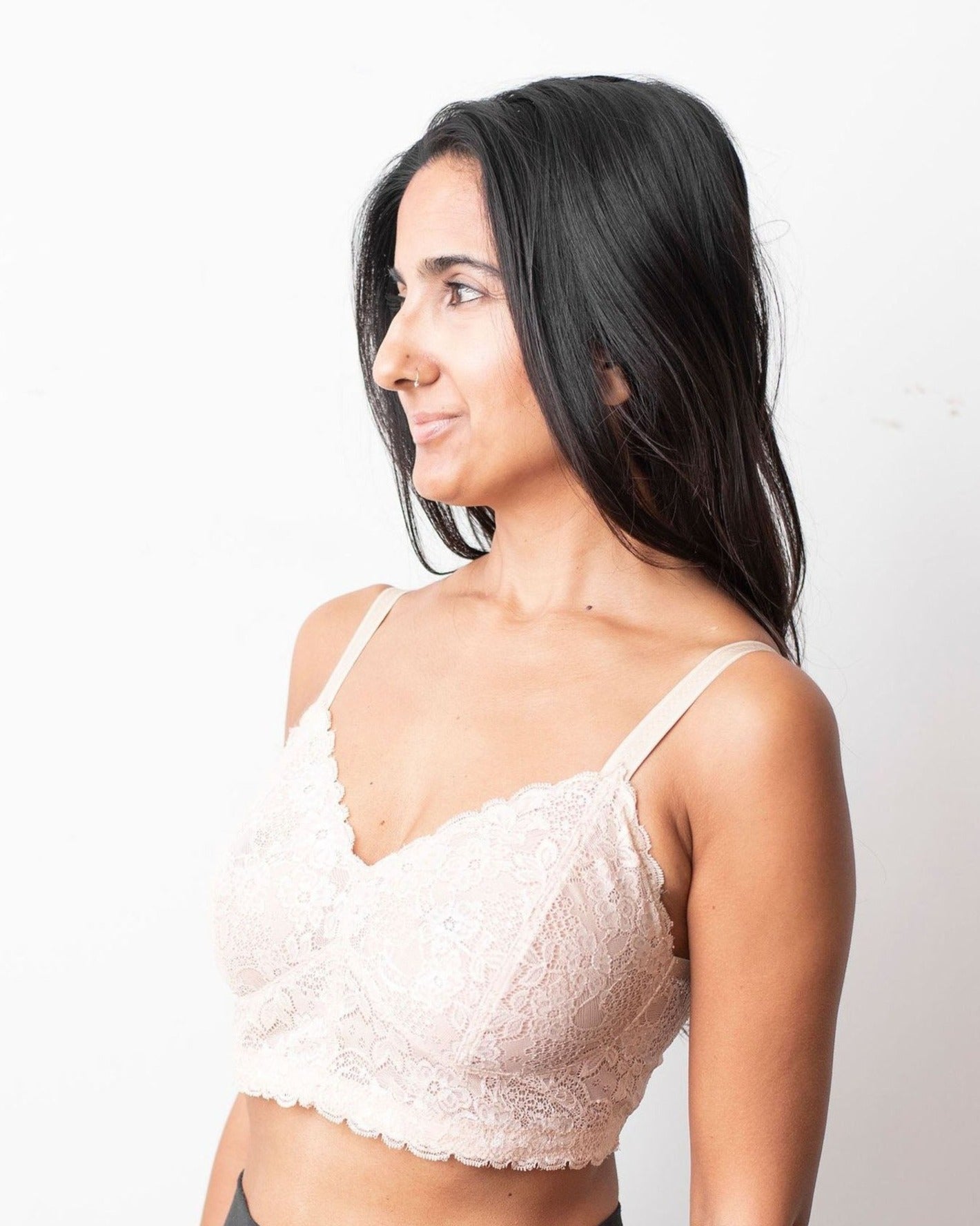 Model with long black hair is wearing an beige wire free, scalloped bra. Shot from the side.